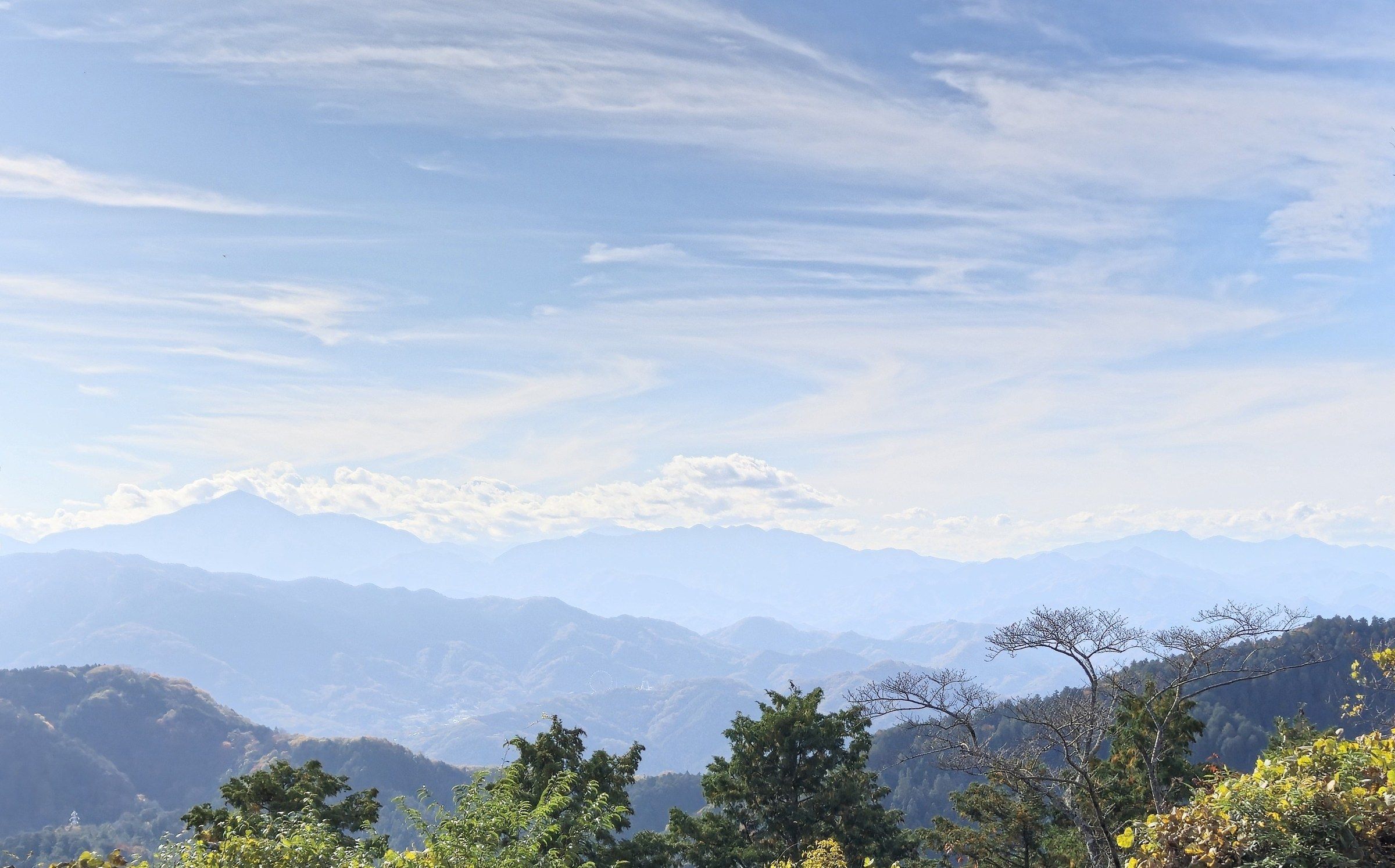 A photo of forested mountains under a blue sky with thin clouds.