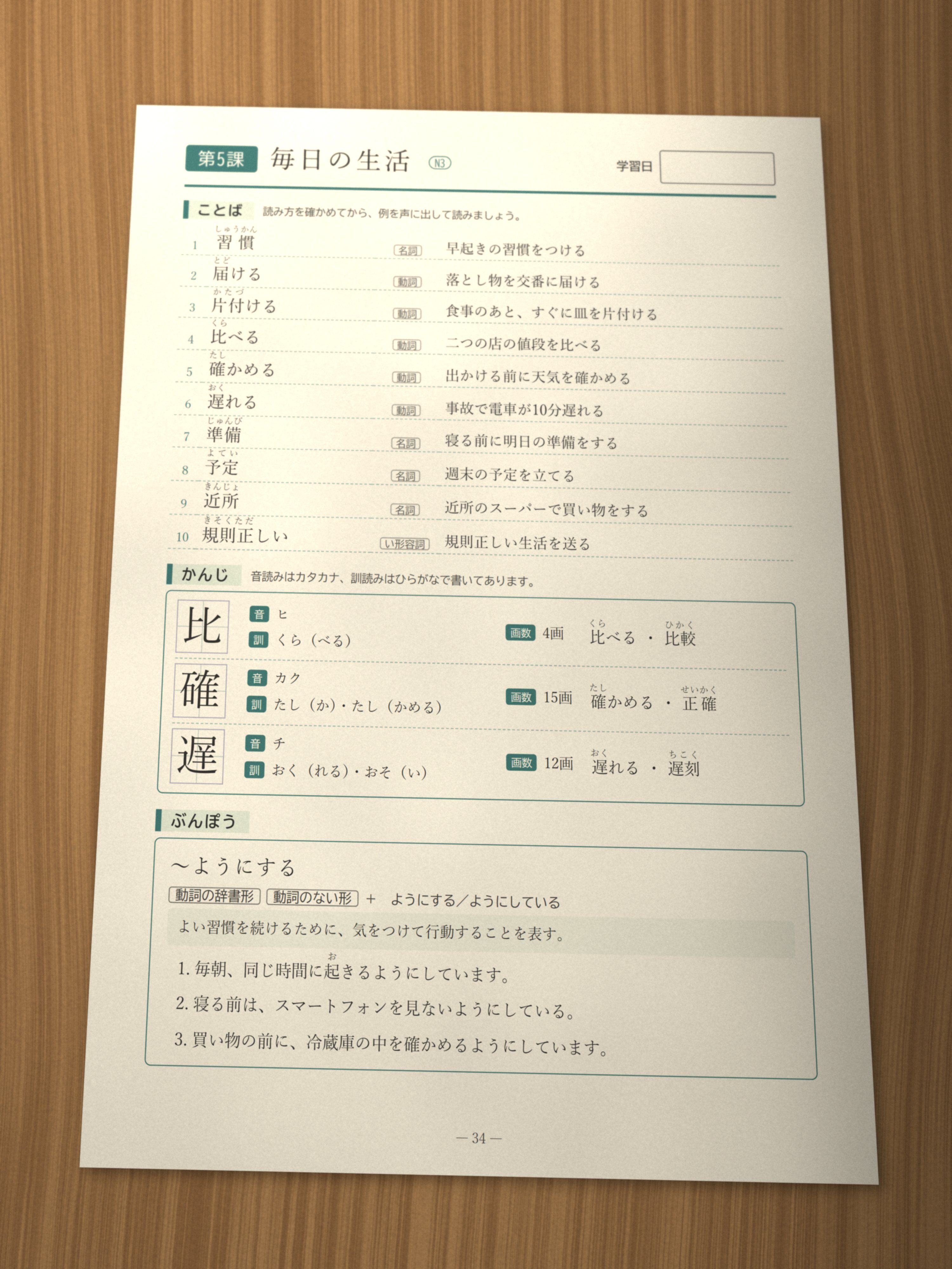 A printed Japanese study page on a wooden desk: Lesson 5, Daily life (N3), with ten vocabulary words and example sentences, three kanji with their readings, and the grammar pattern 〜ようにする with three examples.