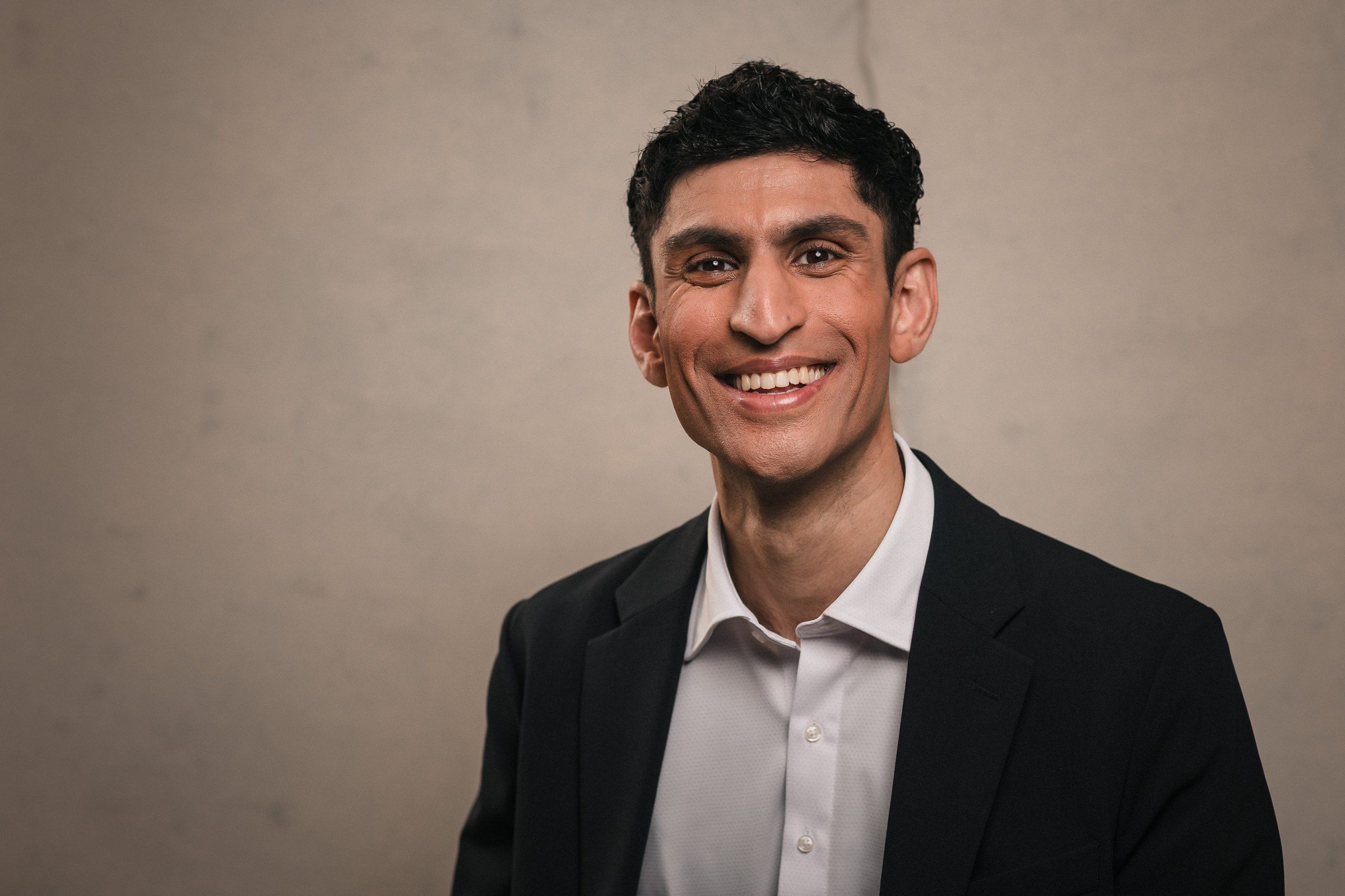 Rounak Zoeb smiling, wearing a dark blazer and open-collared white shirt.