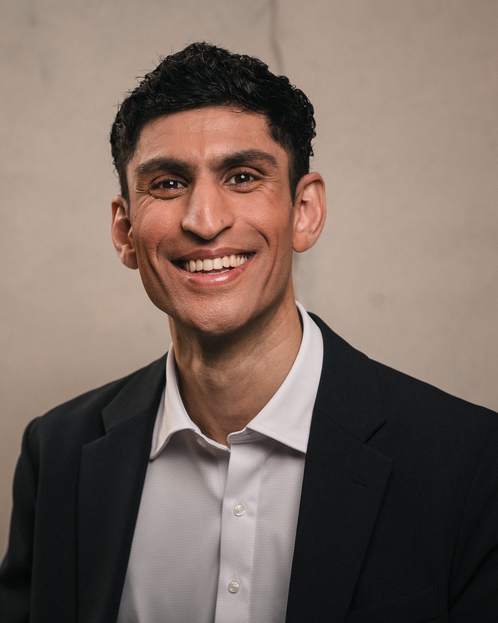 Rounak Zoeb smiling, wearing a dark blazer and open-collared white shirt.